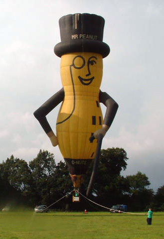 Yellow peanut with black arms, hat, stick and face features, including a smile and a monocle. White gloves. Six black squares on his left front.