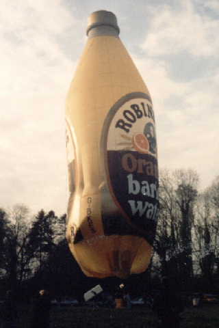 Yellow balloon in the shape of a bottle with a green cap and the Robinsons Orange Barley Water label on the back and front.