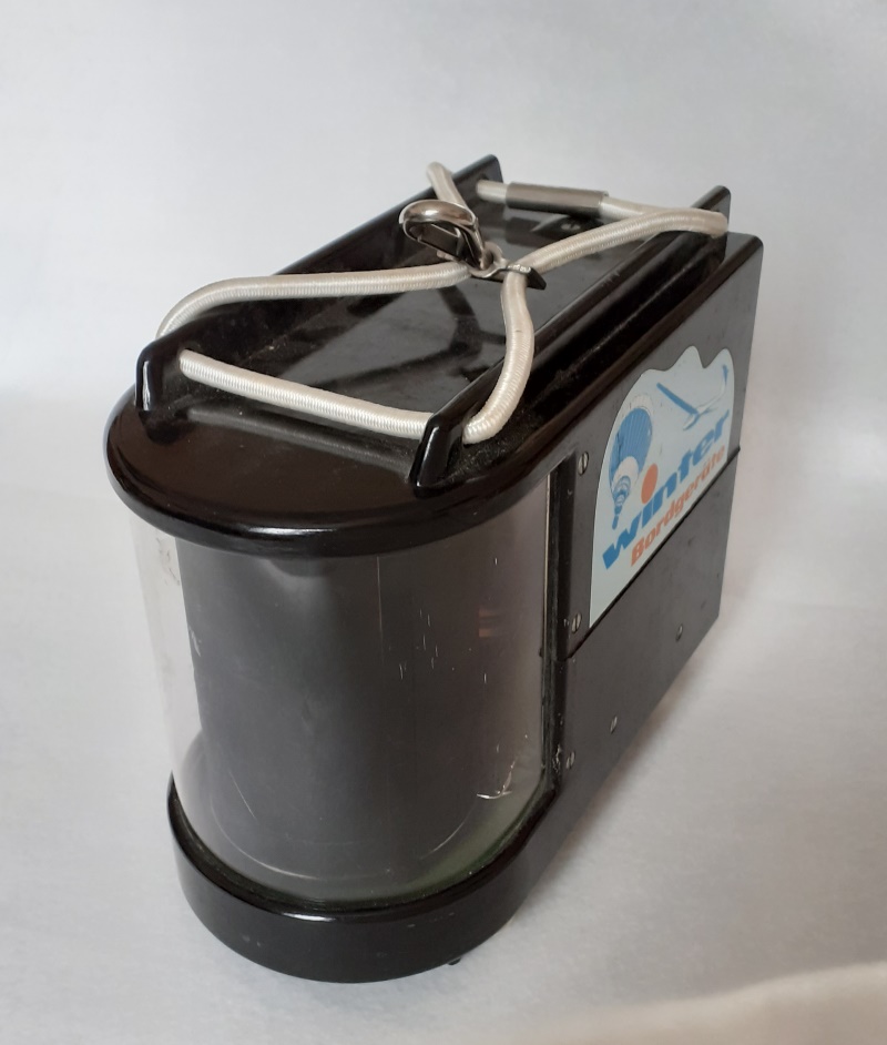 Front view, a black rectangle with a curved clear perspex screen at the front, housing the drum, recording pen and needle. At the top is a thick elasticated cord to secure it in place. 