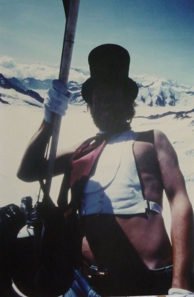 Colour picture of Robin Batchelor standing in a basket whilst flying over the Eiger mountain wearing victorian top hat dressed as Jules Verne fictional character Passpartout