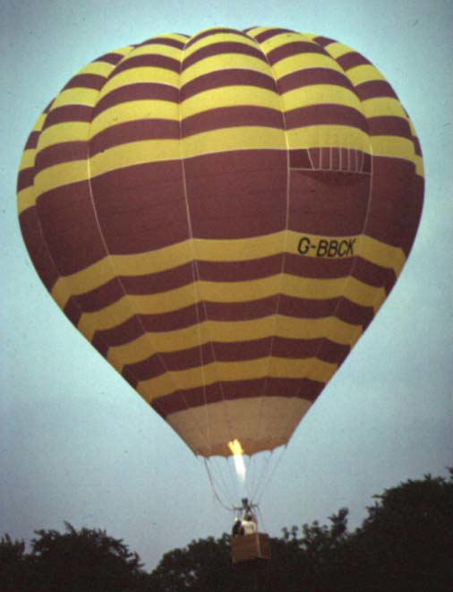 Balloon with thin purple and yellow horizontal stripes, pictured having just launched