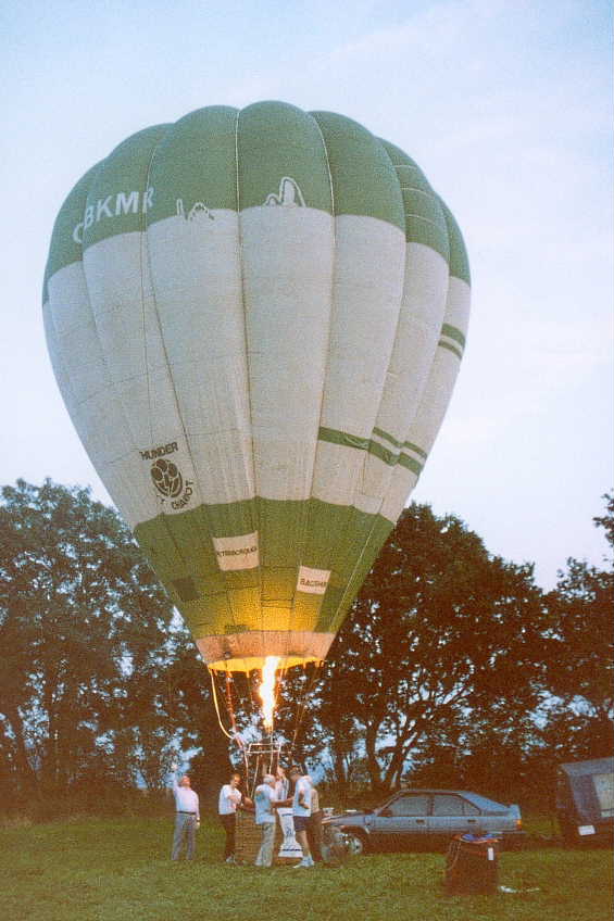 Green top, white thick middle band, green base. Thunder Sky Chariot logo at base of white band comprising a black circle with 3 round clouds and a lightning streak from middle cloud. Burner is lighting base of balloon.