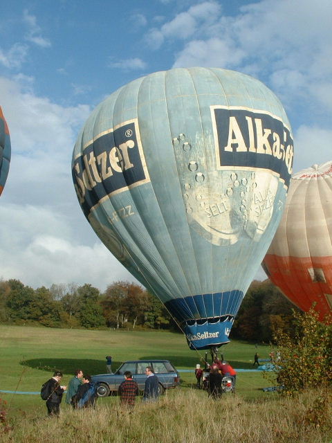 Light blue balloon with Alka Seltzer in white lettering in a black rectangle below which are two large Alka Seltzer tablets partly dissolved and fizzing.