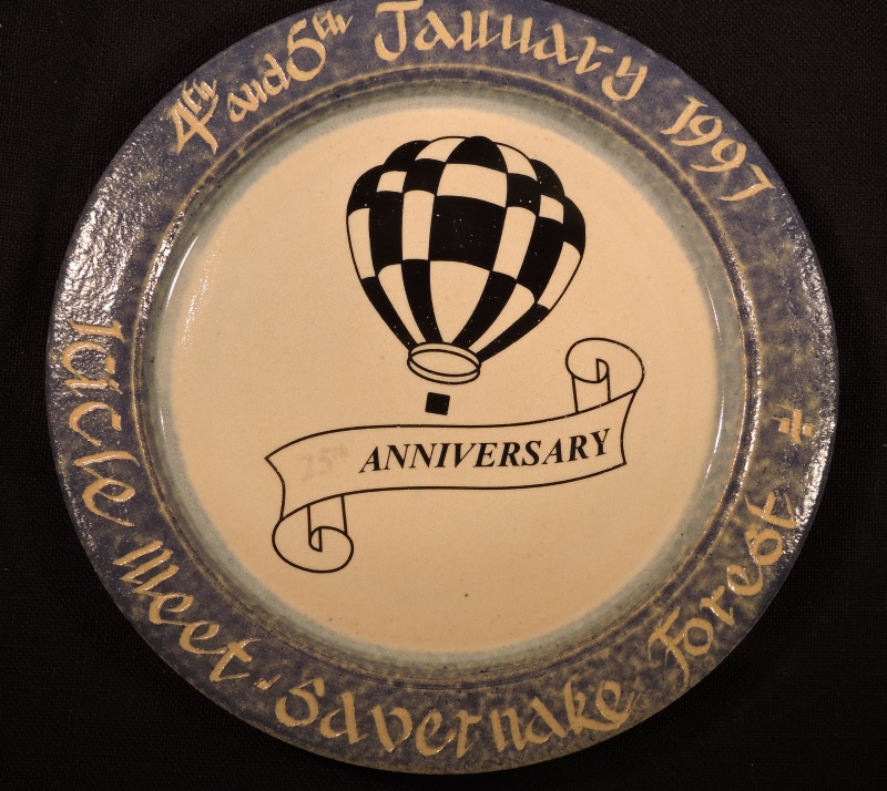 White ceramic plate with blue grey rim with event details in cream on the rim. The centre has an image of a black and white chequered balloon. Underneath is a black and white banner with 25th Anniversary