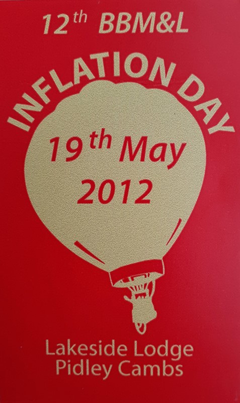 Red background to sticker with a buff silhouette of a balloon in the centre and event date across the balloon. At foot of sticker is the location.