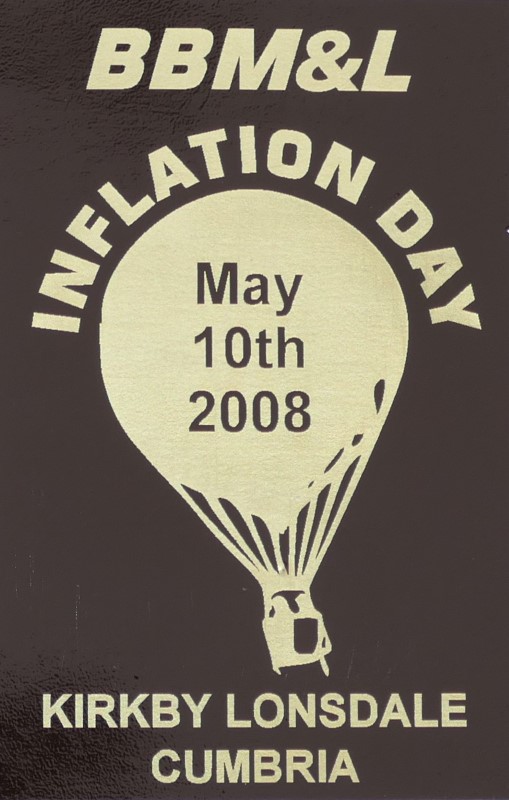 Black background to sticker with a buff silhouette of a balloon in the centre and event date across the balloon. At foot of sticker is the location.