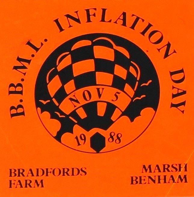 Dayglow orange background to sticker with a black silhouette of a balloon in a circular background in the centre and event date across the balloon. At foot of sticker is the location.