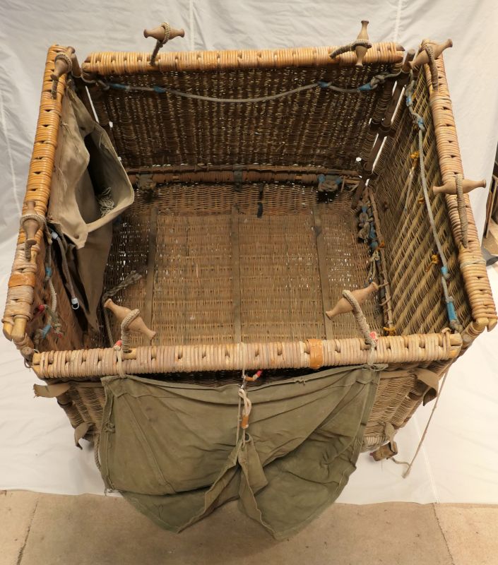 Looking down into a square folding wicker basket, showing the wicker floor and a canvas bag attached to one side for holding loose sand.  
