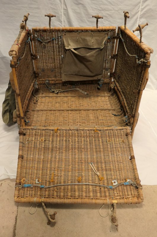  Image looking into a square folding wicker basket through one dropped side. Each side has 2 wooden toggles for attaching the basket to the load ring.   