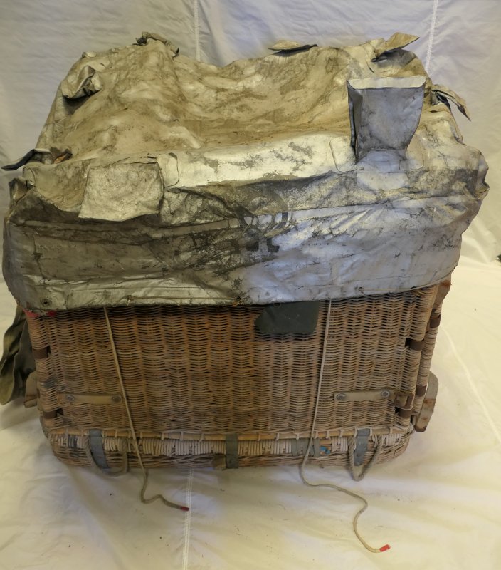 Folding square wicker basket fully built and the top covered by a silver cover with the Omega logo.