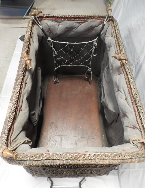 Looking into basket from short edge. There is a wooden floor. The grey fabric lining has a large pocket sewn into it each long side, for maps etc, and there is a mesh on the short edge to secure stowed items.