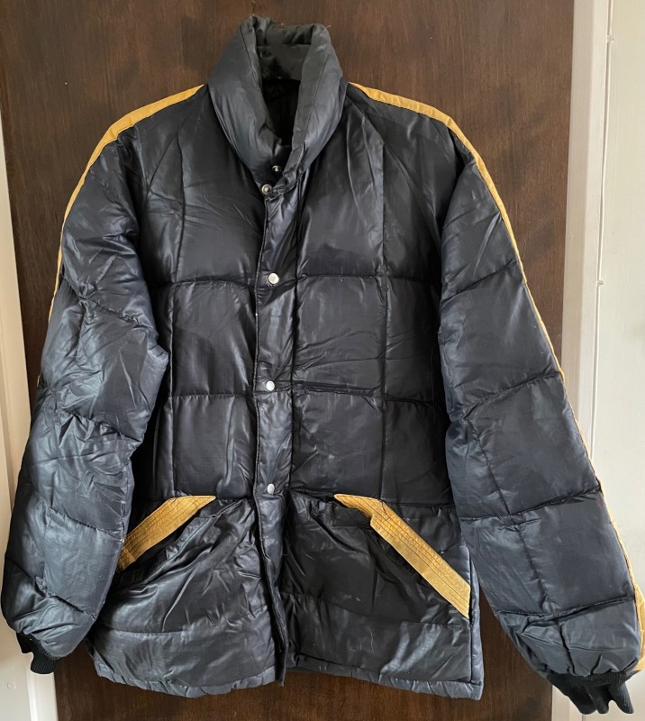 Black padded jacket with orange stripe down the sleeves and across the top of the 2 pockets. 