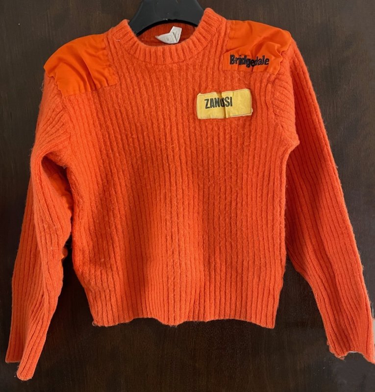 Military style orange jumper with patches on the shoulders and elbows. Manufacturers name on left chest and below is yellow patch with Zanussi in black lettering.