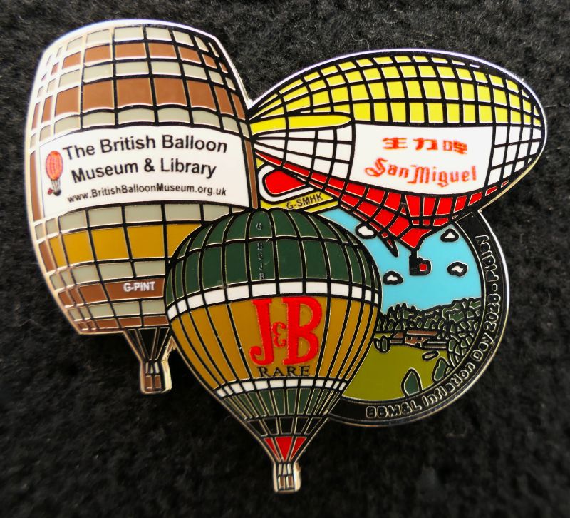 Pin features beer barrel with BBM&L name and website, San Miguel Airship and J&B balloon, all set to left of partly visible green circle depicting location field. Circle is edged in black with event name and year in silver. Outlines are in silver.