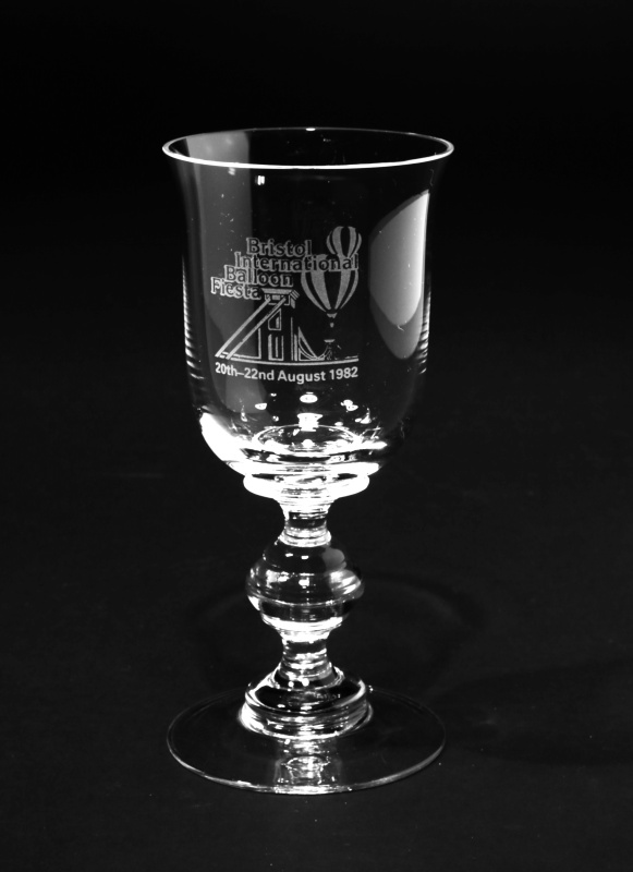 Wine glass with engraved image of Clifton Suspension Bridge with two hot air balloons flying over. Event name and year given.