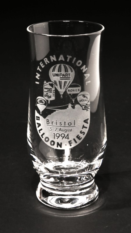 A curved beer glass with Land Rover round, Unipart oil can, Unipart round, Rover round and Jaguar round, balloons flying over image of one end of Clifton Suspension Bridge and trees. Event title surrounds image and event date is at foot of image.