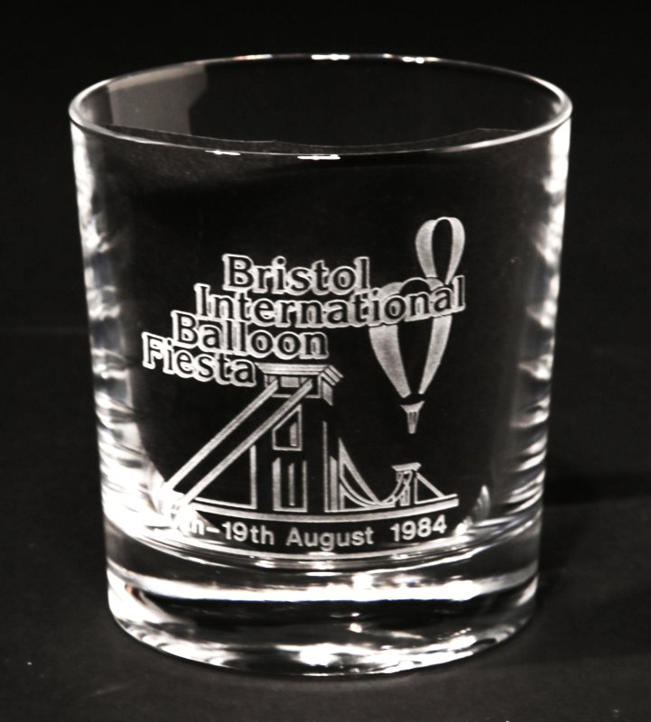 Glass tumbler with simple drawing of 2 balloons over Clifton Suspension bridge and text ‘ Bristol International Balloon Fiesta 17-19 August 1984’ all in white.