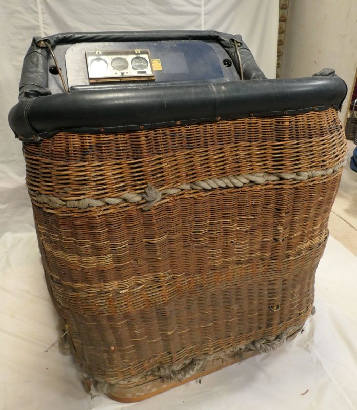  brown wicker basket with a black leather rim and an instrument panel fitted to one of the short edges. The basket has 4 flying wires. 