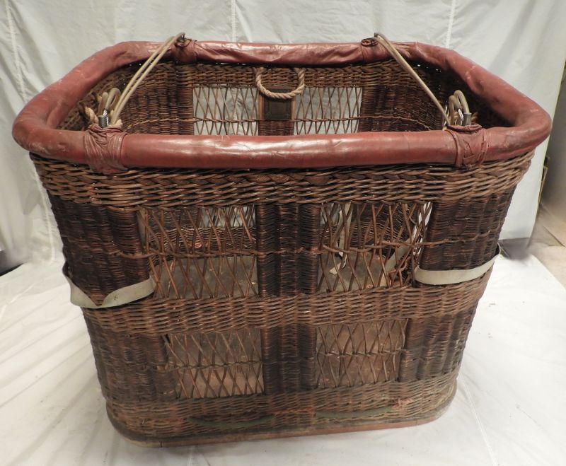 Wicker basket with red leather roll top. The wicker has 4 open weave panels on the long sides and 2 on the short sides. There are 8 flying wires.   