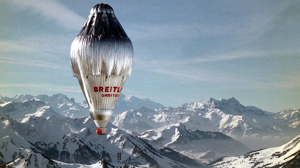 Colour picture of silver coloured balloon flying above snow-covered mountains